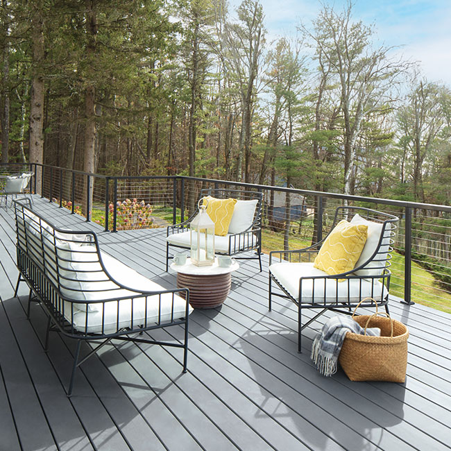 A set of black metal outdoor furniture with white cushions and yellow pillows on a spacious silvery blue stained deck. A set of black metal outdoor furniture with white cushions and yellow pillows on a spacious silvery blue stained deck.