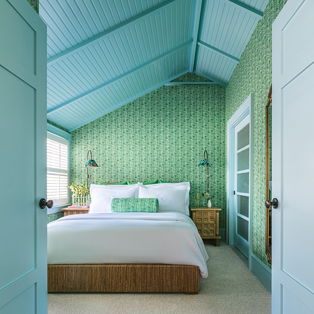 A bedroom with a sky blue painted shiplap vaulted ceiling, trim, and doors, and pretty, green patterned wallpaper. A bedroom with a sky blue painted shiplap vaulted ceiling, trim, and doors, and pretty, green patterned wallpaper.