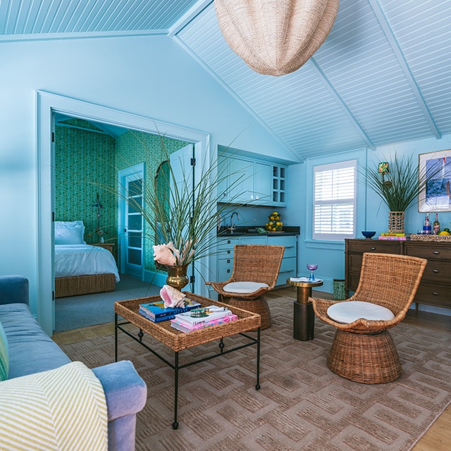 A sky blue painted living room with a shiplap vaulted ceiling and coastal decor, open to a back bedroom with green printed wallpaper. A sky blue painted living room with a shiplap vaulted ceiling and coastal decor, open to a back bedroom with green printed wallpaper.