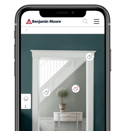 A smart phone with the Benjamin Moore Color Portfolio app showing a dark gray wall with white trim, looking into a light gray hallway with white trim, a white table and green topiary. A smart phone with the Benjamin Moore Color Portfolio app showing a dark gray wall with white trim, looking into a light gray hallway with white trim, a white table and green topiary.