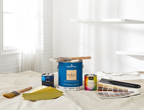 A selection of Benjamin Moore products on a drop cloth, including a gallon of Regal Select, a variety of color samples, two paintbrushes, and a fandeck. A selection of Benjamin Moore products on a drop cloth, including a gallon of Regal Select, a variety of color samples, two paintbrushes, and a fandeck.