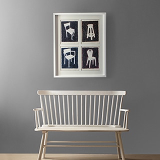 A photograph of different accent chairs hangs in a hallway above a two-person bench.