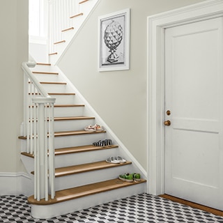 A hallway with a patterened area rug and staircase topped with pairs of shoes on the first four risers.