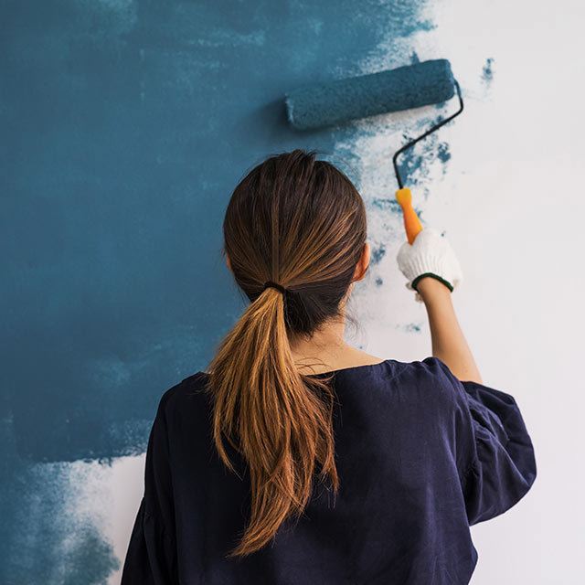 Woman painting a wall blue with paint roller. Woman painting a wall blue with paint roller.