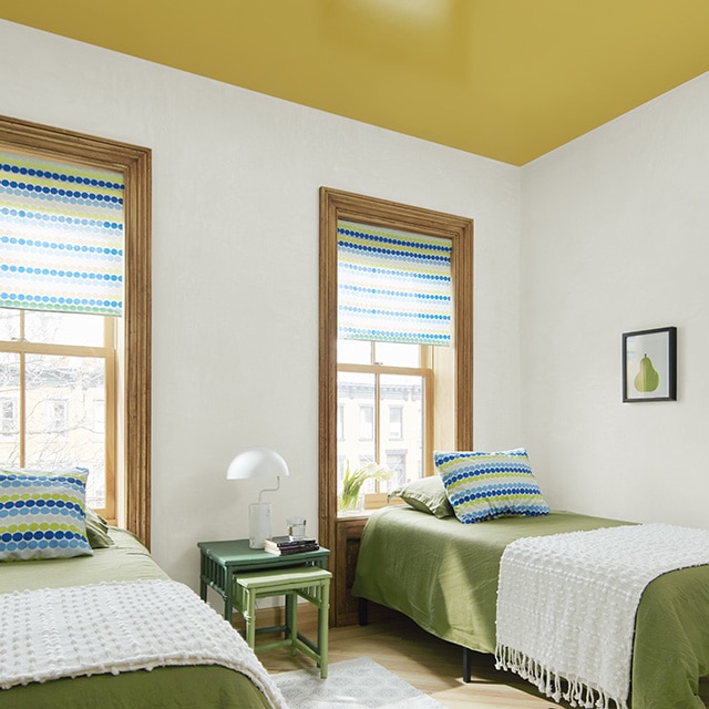 A rich ochre painted ceiling with hints of green and yellow makes a fun statement in this bedroom with white walls, natural wood trim, and twin beds with green and white bedding. A rich ochre painted ceiling with hints of green and yellow makes a fun statement in this bedroom with white walls, natural wood trim, and twin beds with green and white bedding.