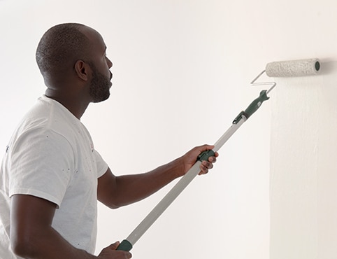 A painting contractor rolling white paint onto a primed wall. A painting contractor rolling white paint onto a primed wall.