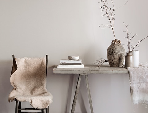 Gray dining area featuring a rustic table with books, vases, and branches, and chair topped with white fur blanket. Gray dining area featuring a rustic table with books, vases, and branches, and chair topped with white fur blanket.