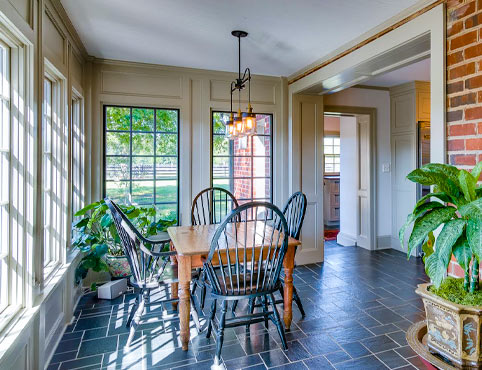 Sunroom with one brick wall and three white-painted walls with large windows, featuring a wooden table and chairs and a variety of plants. Sunroom with one brick wall and three white-painted walls with large windows, featuring a wooden table and chairs and a variety of plants.