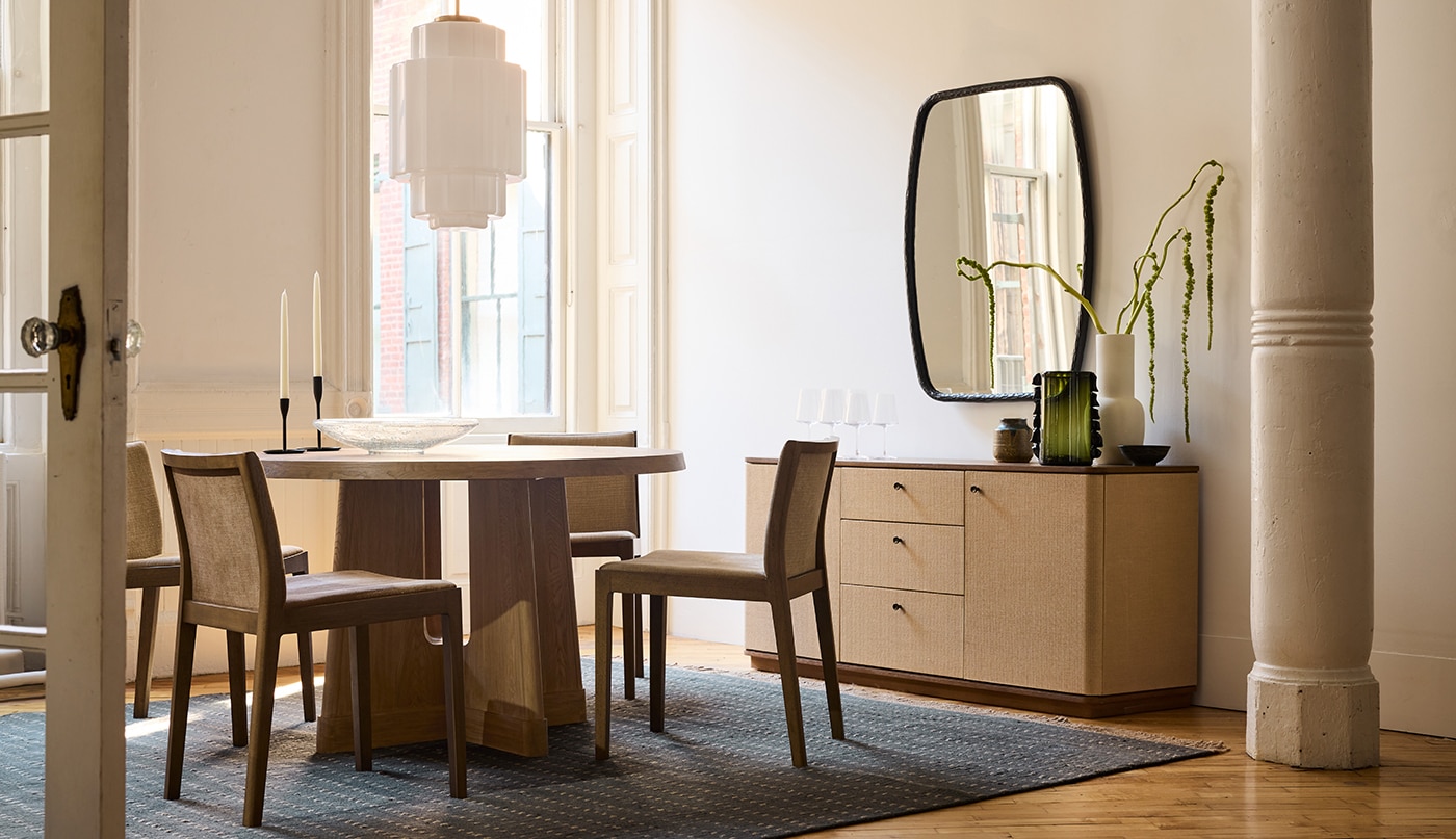 A dining room with neutral painted walls and trim, a wooden table, columns, and a cabinet beneath a mirror.