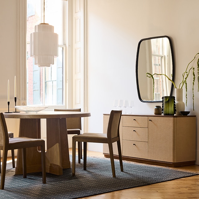 A dining room with neutral painted walls and trim, a wooden table, columns, and a cabinet beneath a mirror.