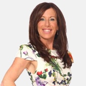 A head shot of a Caucasian woman with brown hair wearing a white short sleeve blouse with green, purple, and red flowers.