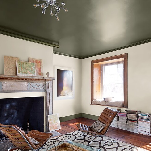 A cozy, sunlit living room with white-painted walls, a dark green ceiling and trim, leather chairs and printed rug, a wood mantel, window trim and door. A cozy, sunlit living room with white-painted walls, a dark green ceiling and trim, leather chairs and printed rug, a wood mantel, window trim and door.