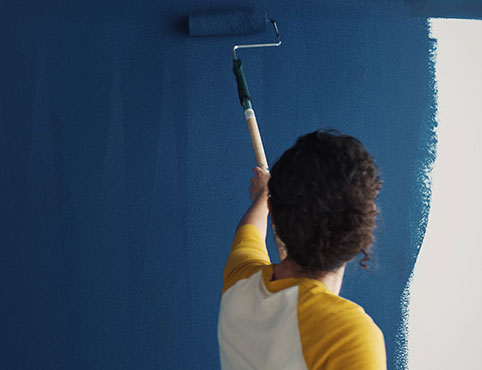 A homeowner uses a roller to paint Symphony Blue 2060-10 on a wall. A homeowner uses a roller to paint Symphony Blue 2060-10 on a wall.