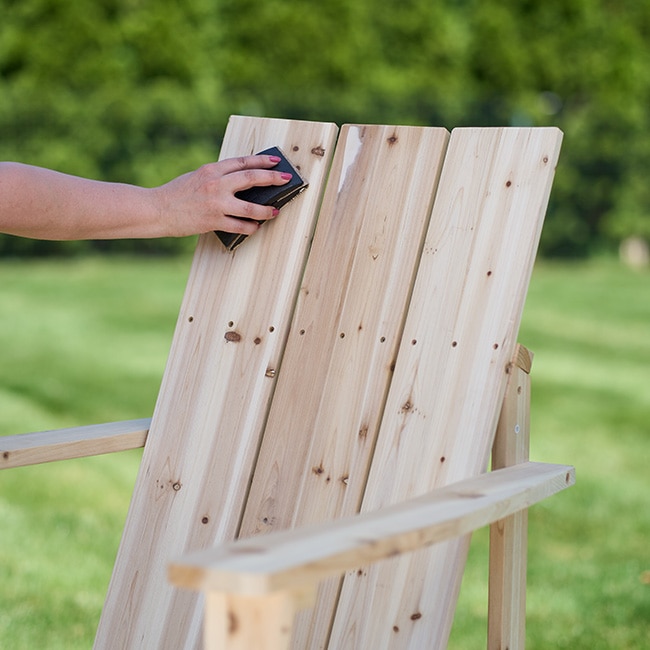 A closeup of someone sanding a wooden Adirondack chair. A closeup of someone sanding a wooden Adirondack chair.