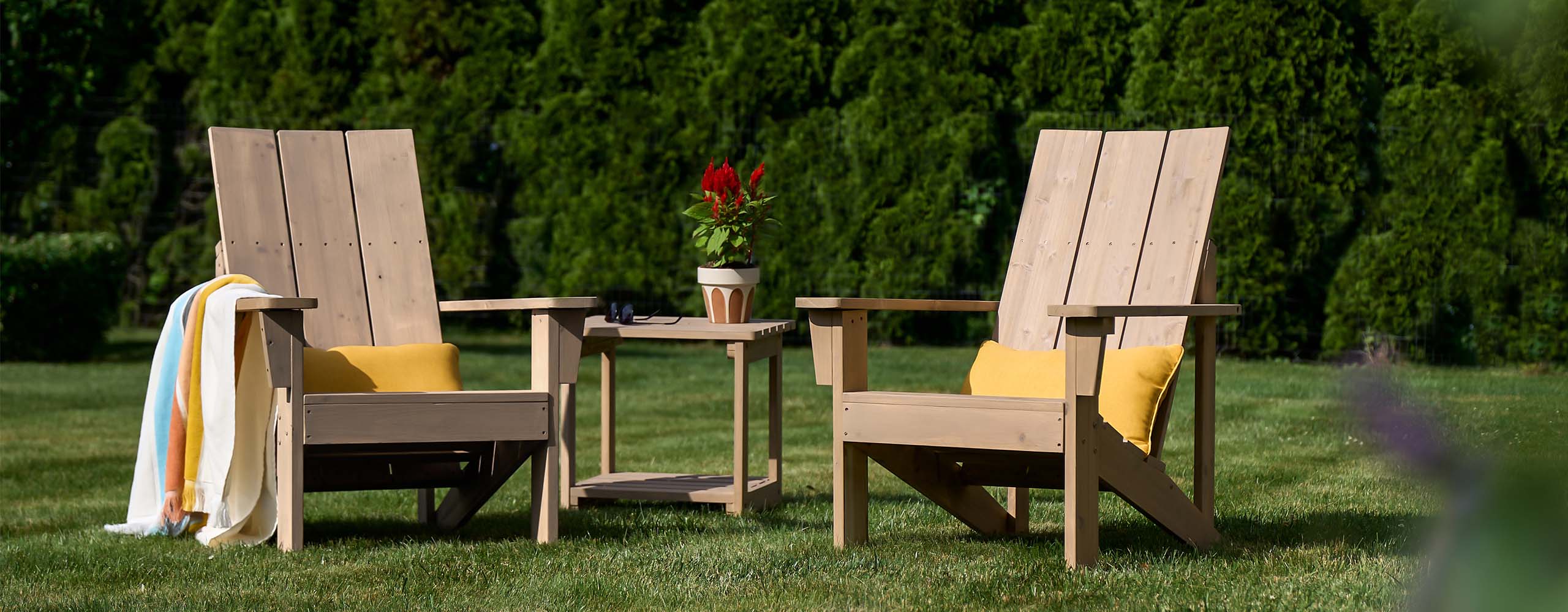 Two lightly stained wooden Adirondack chairs and a wood table sitting on a lush green lawn. Two lightly stained wooden Adirondack chairs and a wood table sitting on a lush green lawn.