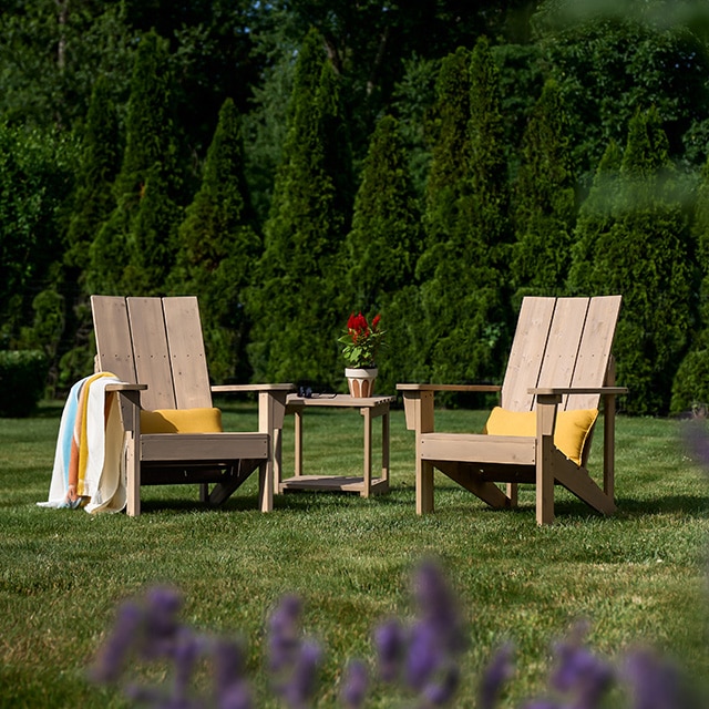 Two lightly stained wooden Adirondack chairs and a wood table sitting on a lush green lawn. Two lightly stained wooden Adirondack chairs and a wood table sitting on a lush green lawn.