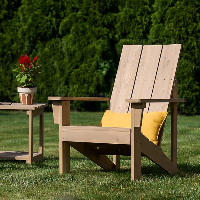 A lightly stained wooden Adirondack chair and a wood table sitting on a lush green lawn. A lightly stained wooden Adirondack chair and a wood table sitting on a lush green lawn.