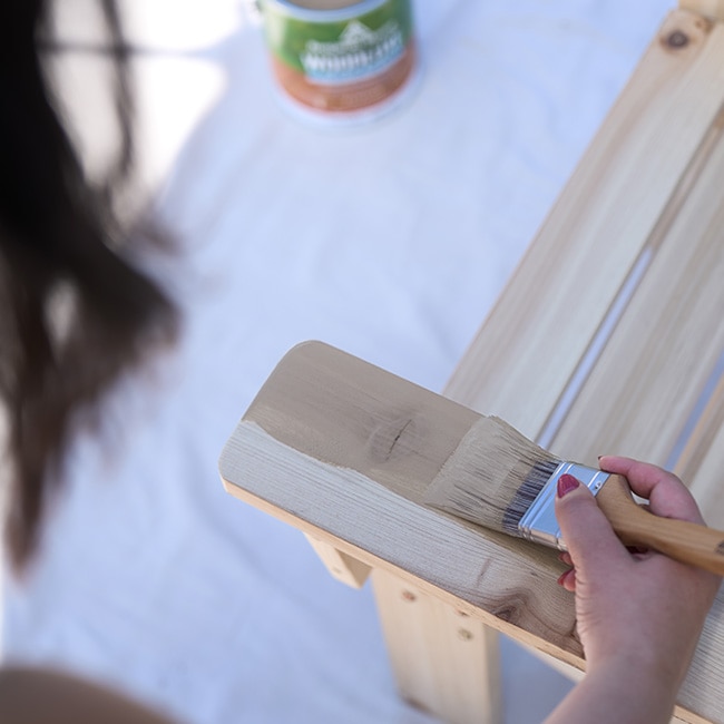 A closeup of someone applying exterior stain to a wooden chair. A closeup of someone applying exterior stain to a wooden chair.