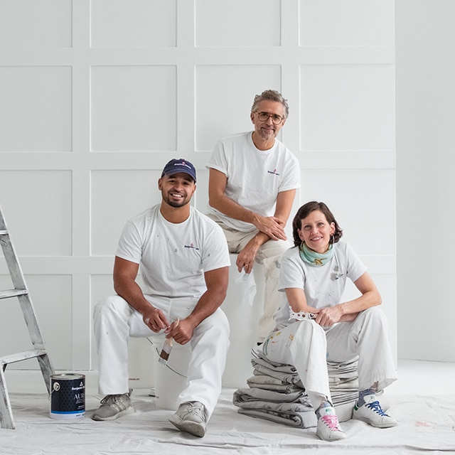 Three Benjamin Moore painting contractors dressed in white, posing in a white-painted room. Three Benjamin Moore painting contractors dressed in white, posing in a white-painted room.