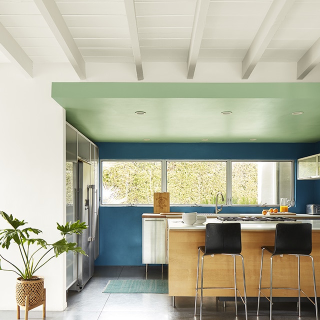 A white painted shiplap ceiling with beams and a white wall leading to a modern kitchen with blue painted walls and a green ceiling. A white painted shiplap ceiling with beams and a white wall leading to a modern kitchen with blue painted walls and a green ceiling.