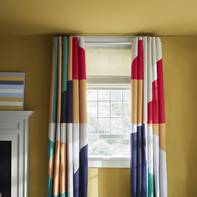 A rich ochre painted wall and ceiling with hints of green and yellow, a white fireplace mantel and trim, and colorful patterned curtains. A rich ochre painted wall and ceiling with hints of green and yellow, a white fireplace mantel and trim, and colorful patterned curtains.