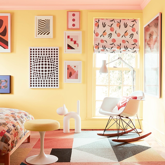 A bright, cheerful kid’s bedroom with yellow painted walls, a pastel pink ceiling, colorful framed artwork, modern furniture, a multicolor bedspread, and geometric print rug. A bright, cheerful kid’s bedroom with yellow painted walls, a pastel pink ceiling, colorful framed artwork, modern furniture, a multicolor bedspread, and geometric print rug.